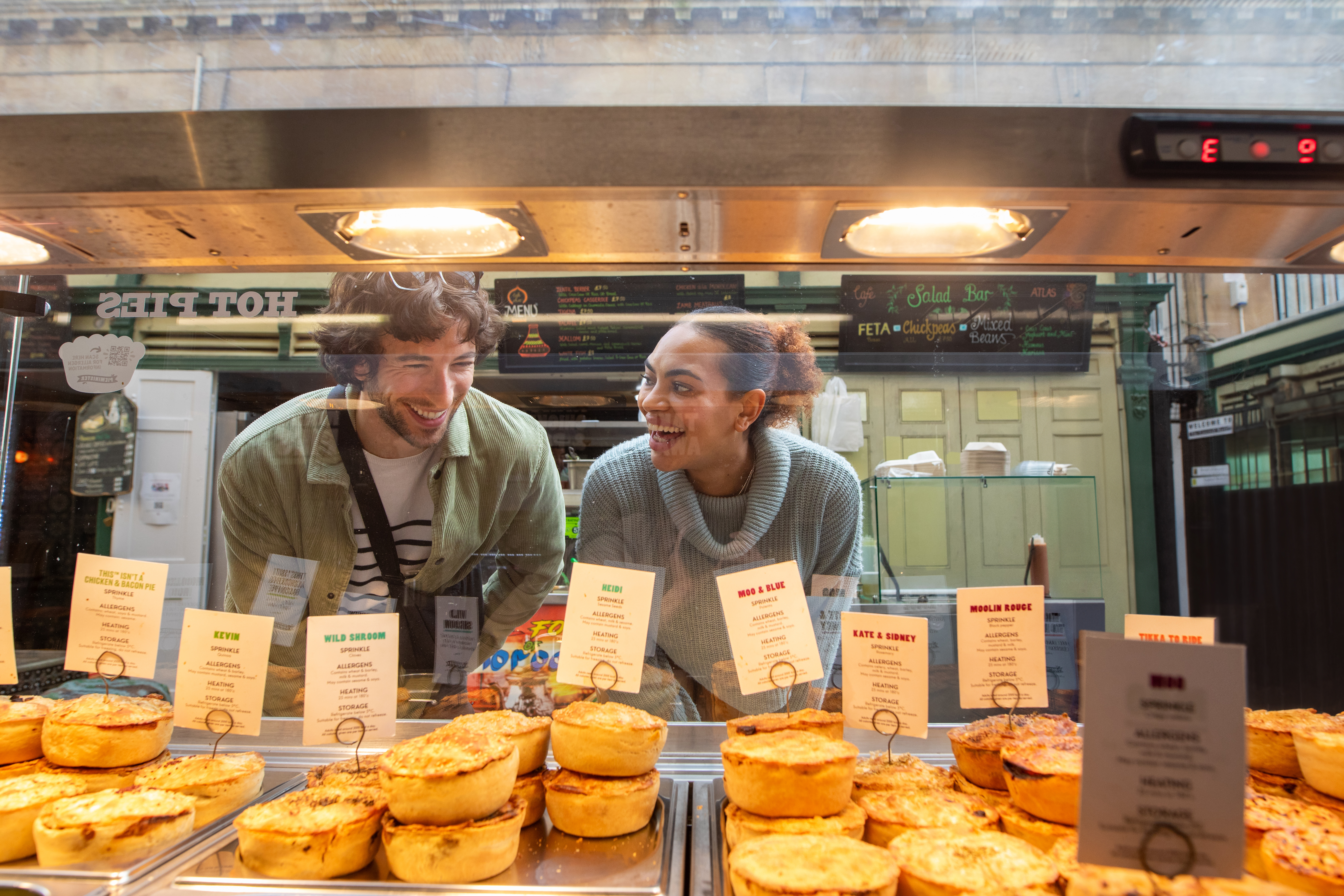 Friends admiring bakery pies through a glass divider.