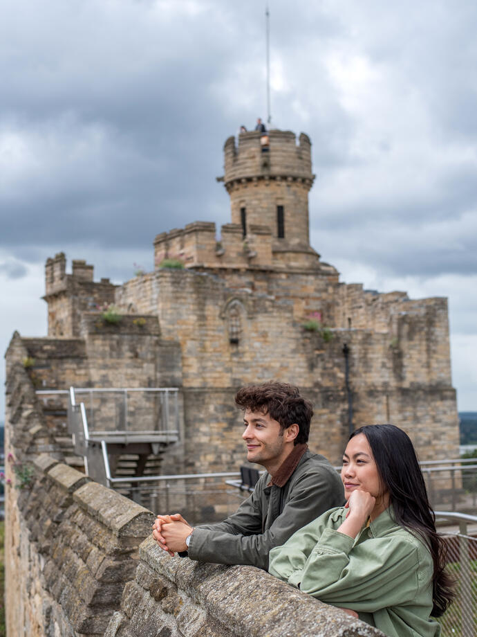 A man and a woman look out to a view from a castle