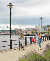 Two people cycling and skateboarding on a path along the River Tyne in Newcastle.
