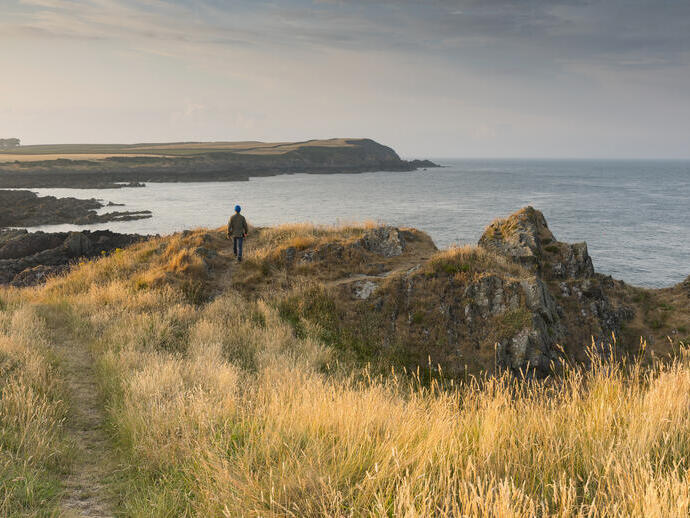 Persona caminando por un sendero costero con vistas a una bahía