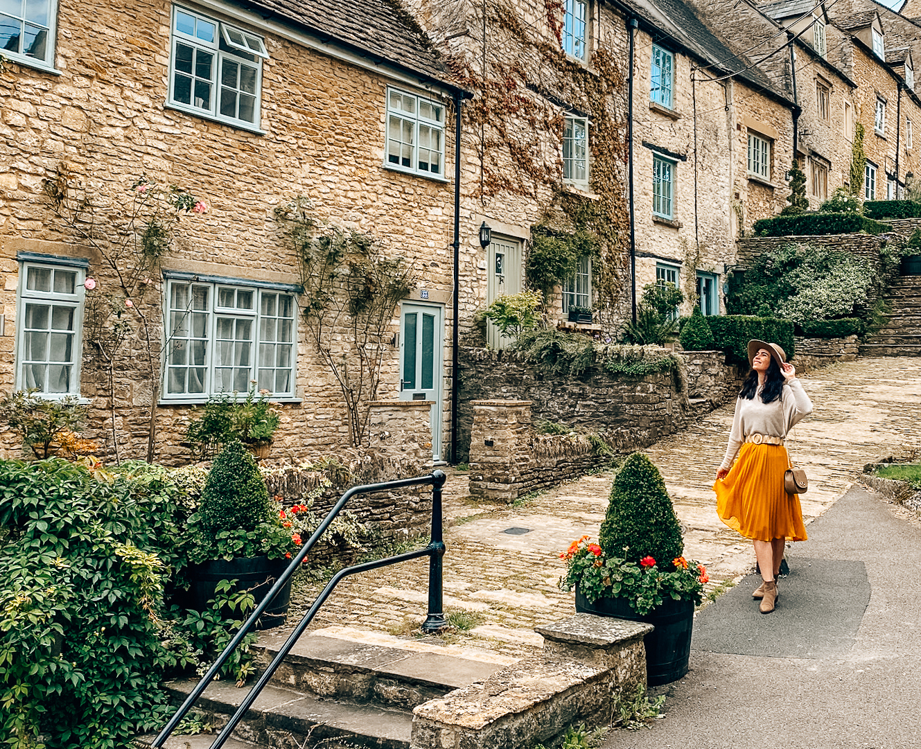 A woman in a hat walks down a steep pebbled footpath in a quaint village.