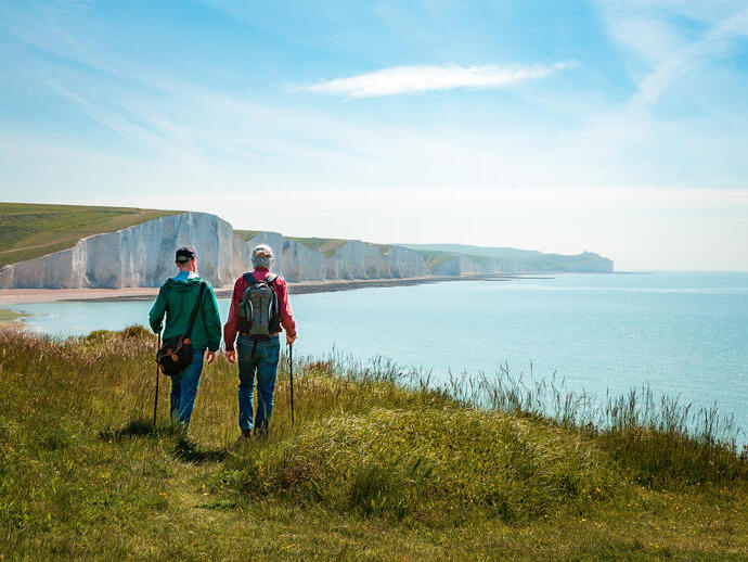 Two men hiking together with the stunning backdrop of white cliffs overlooking the ocean.