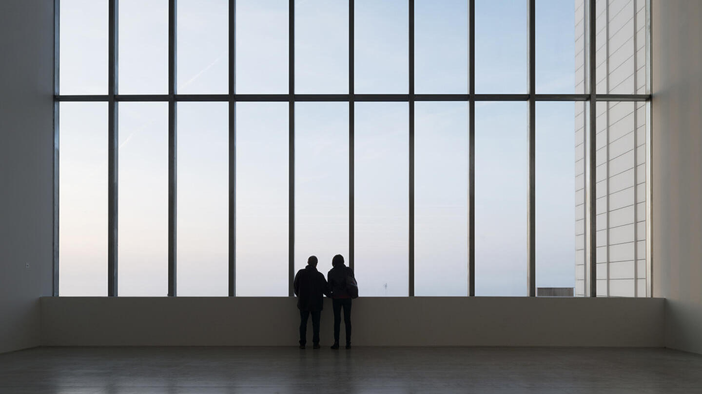Due persone in silhouette che guardano fuori da un'ampia finestra in un edificio contemporaneo