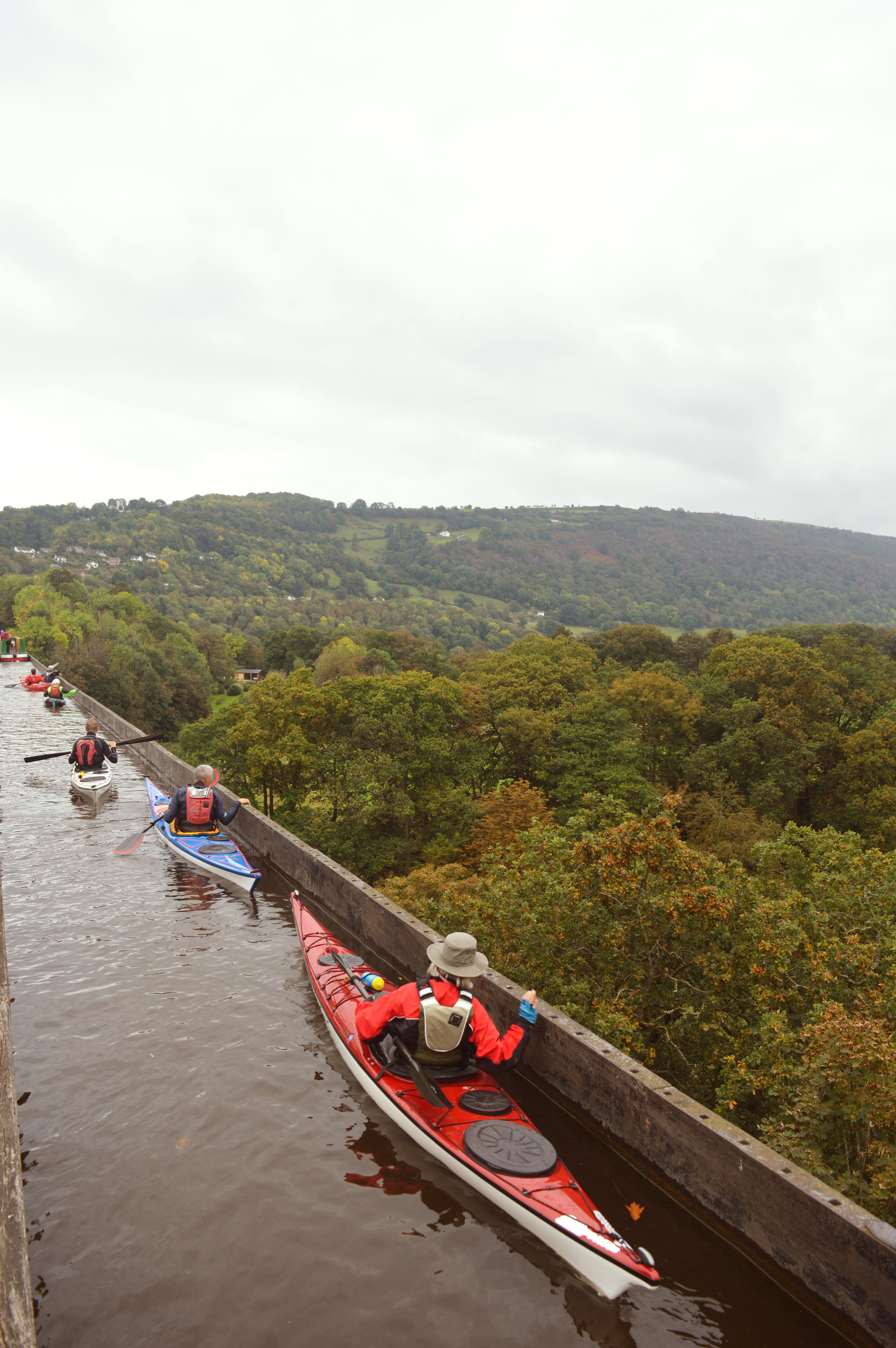 People kayaking across an elevated aqueduct with views of the valley below.