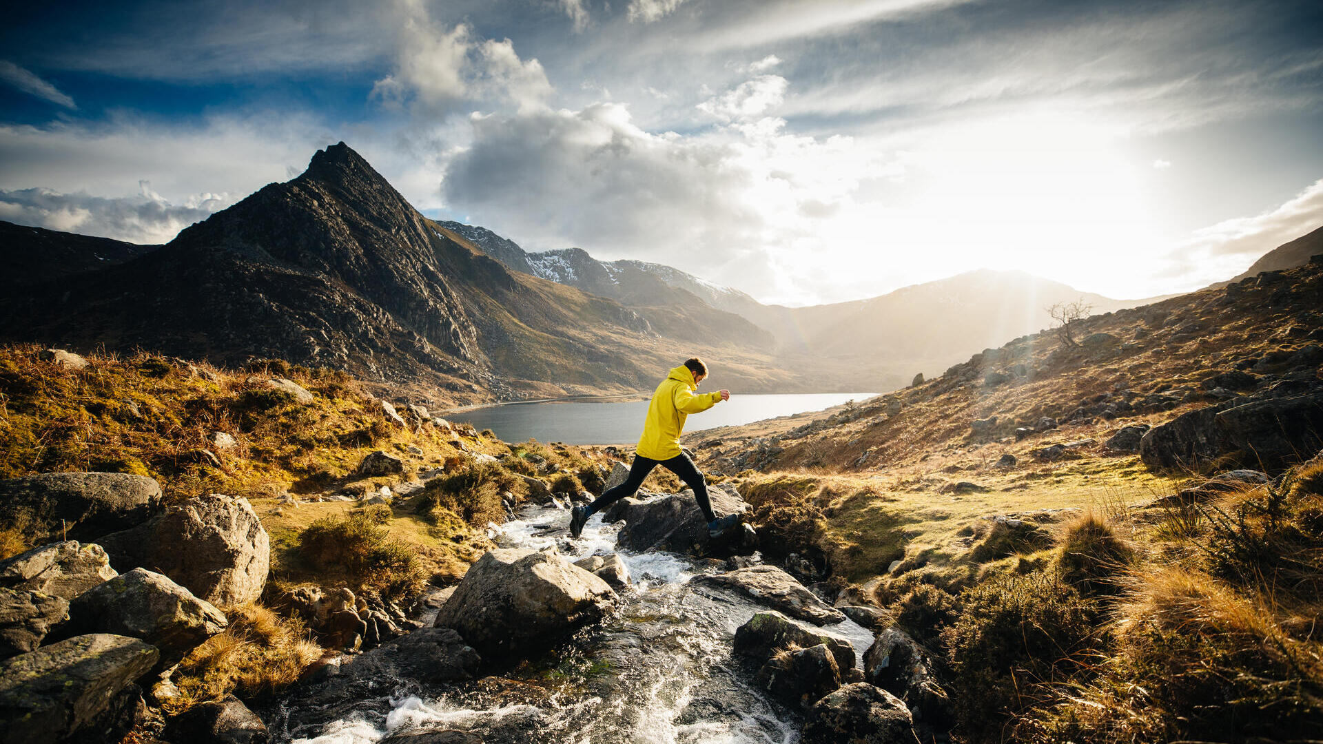 Man jumping from rock to rock across a stream flowing into a lake