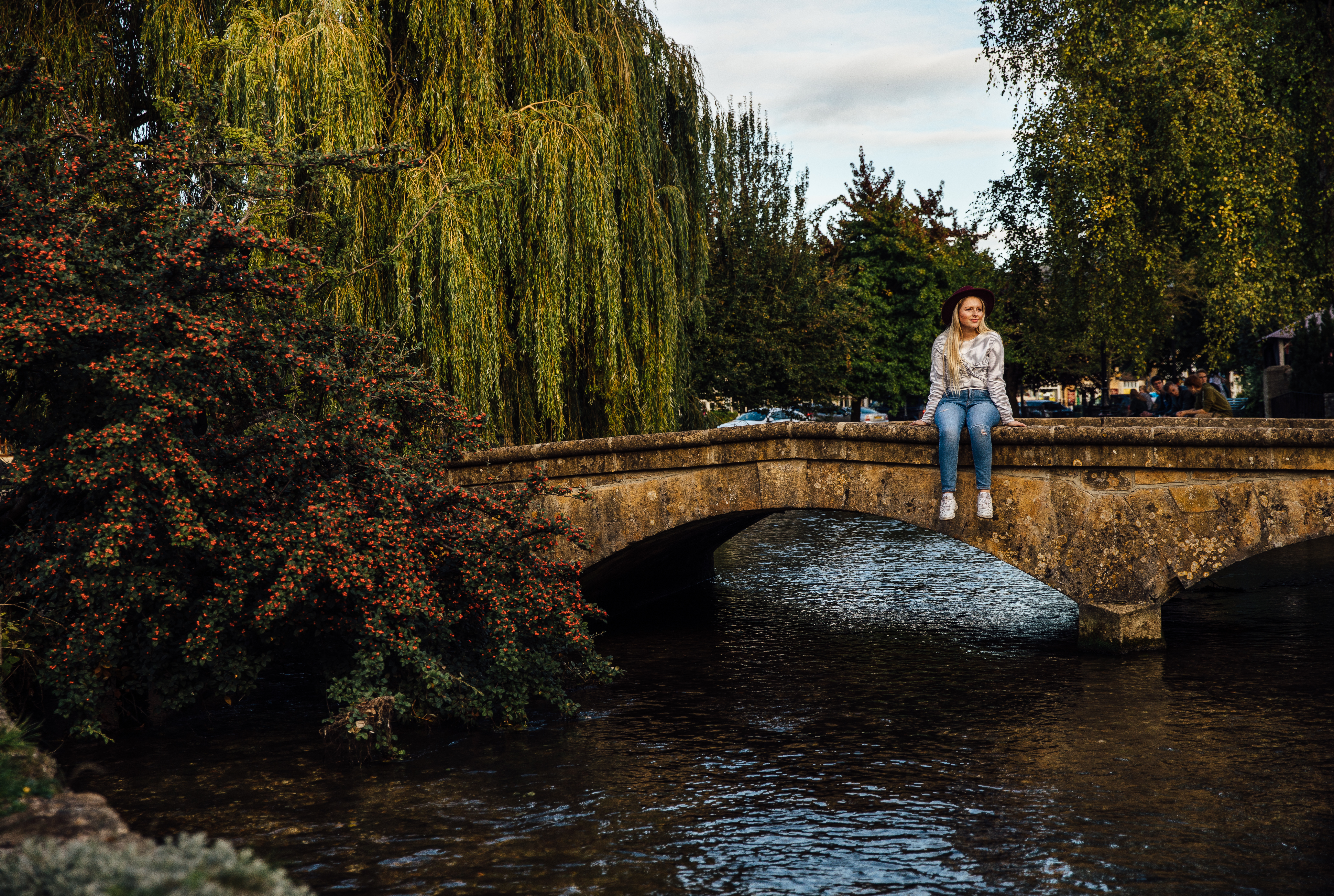 Woman sitting on low bridge over a river in a village