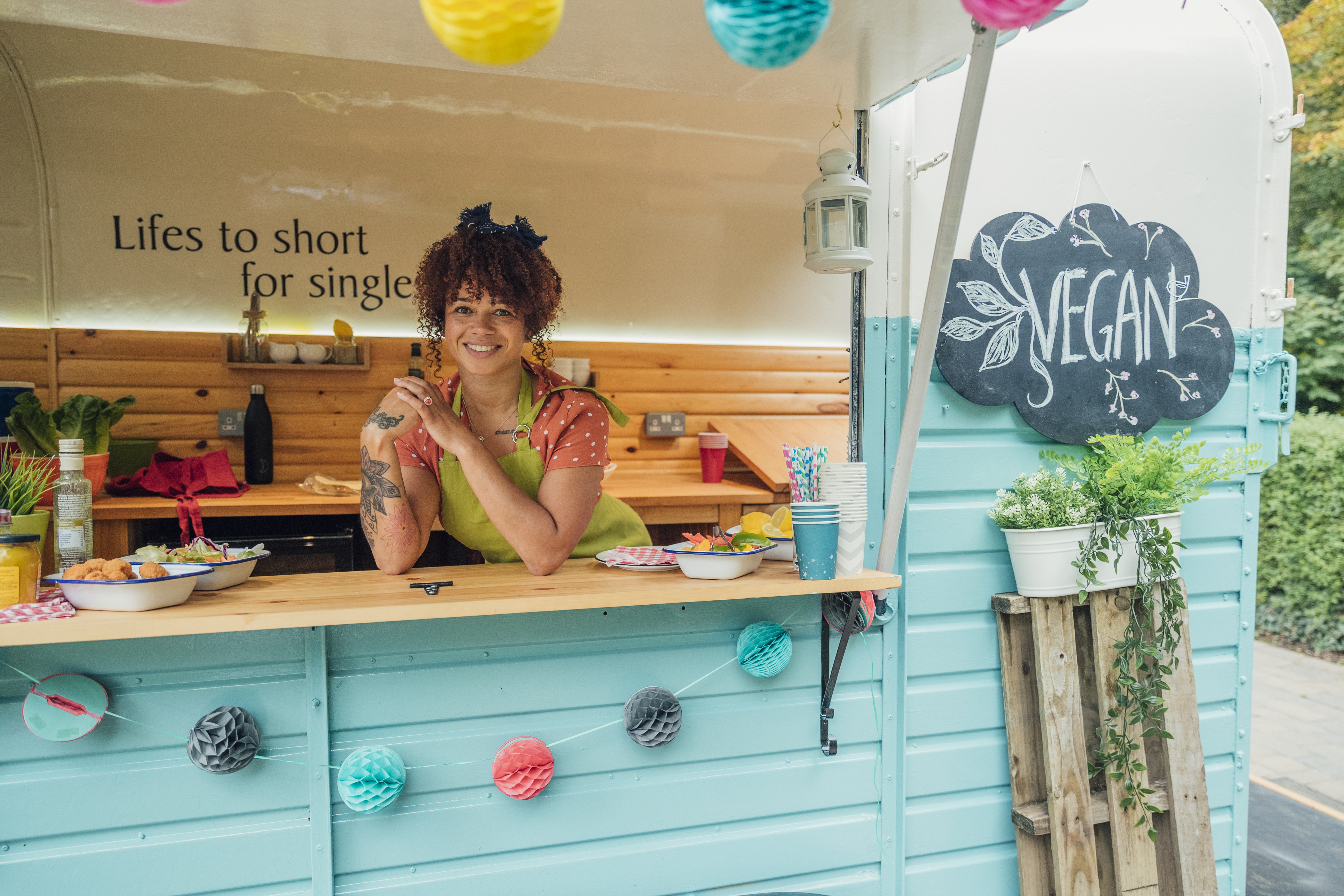 Young woman stood in the hatch of a food truck smiling, ready to serve