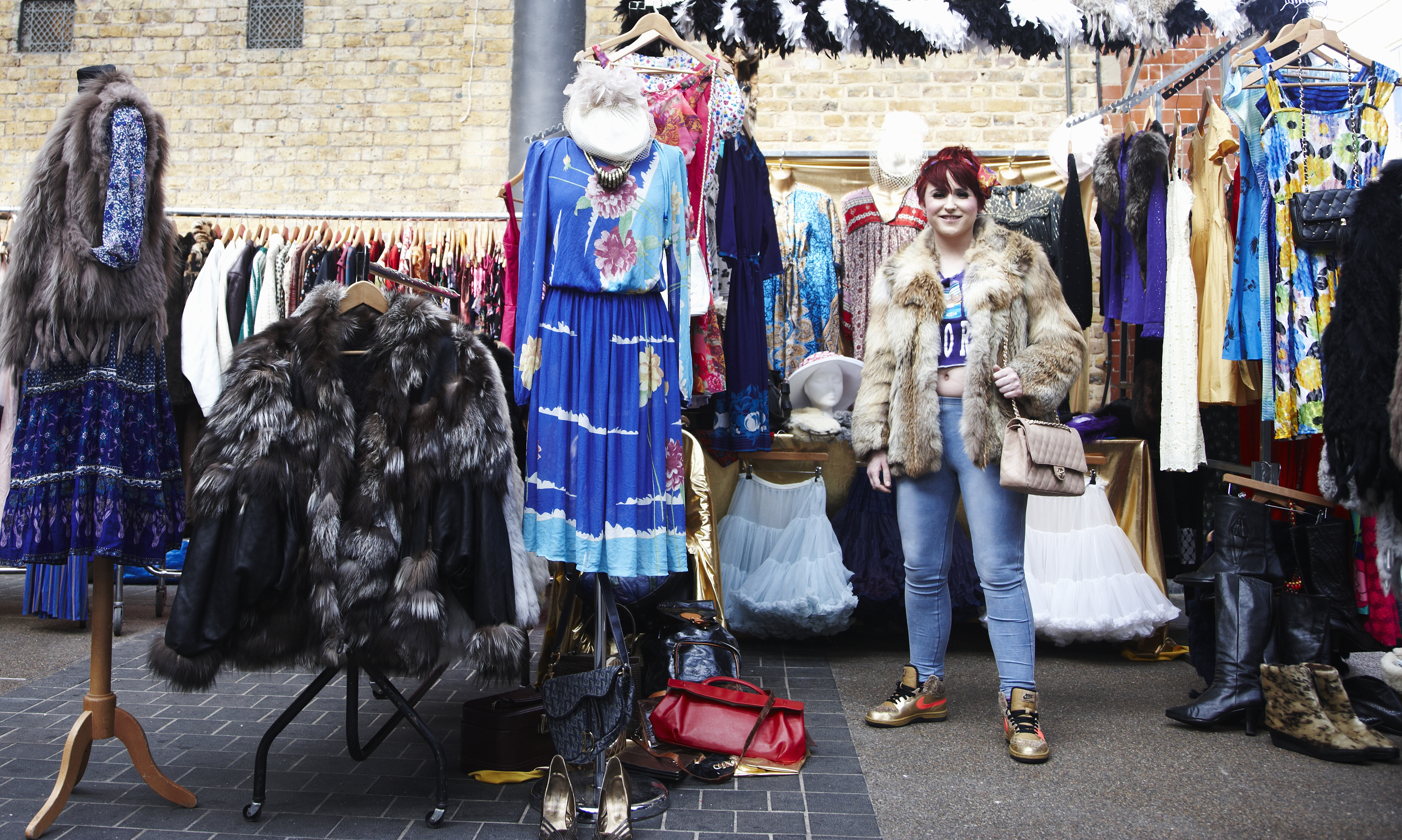 Woman standing by a vintage clothing market stall.