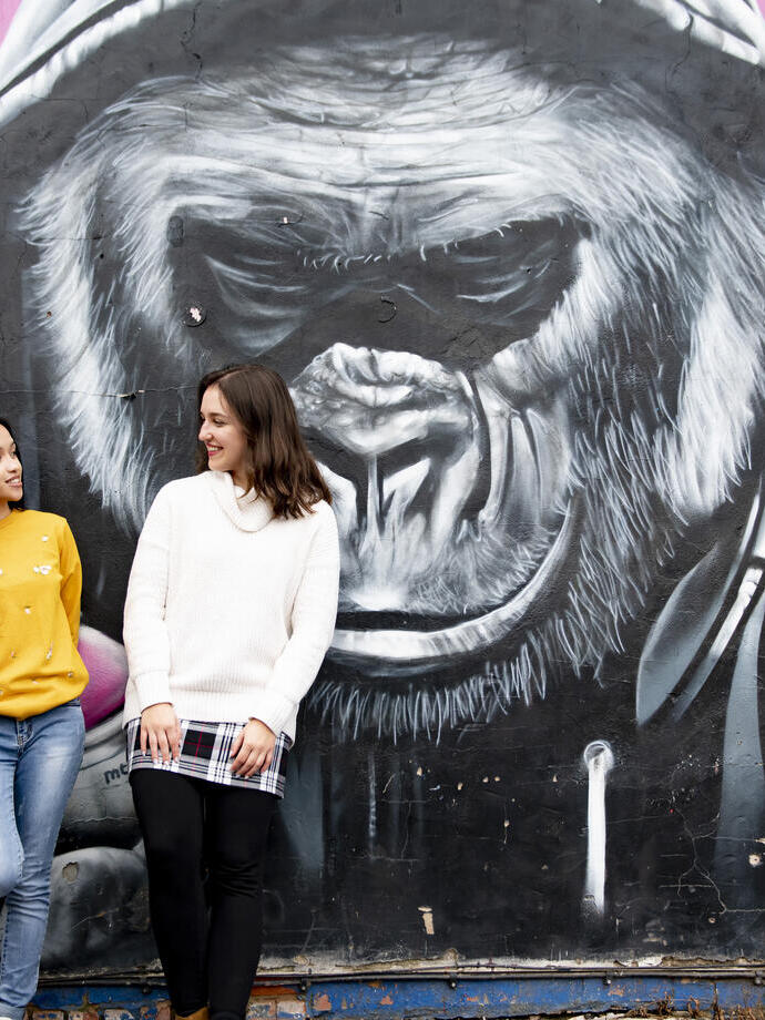 Two women standing in front of painted mural on street wall