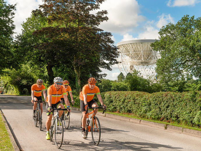 A group of cyclists cycle passed Jodrell Bank