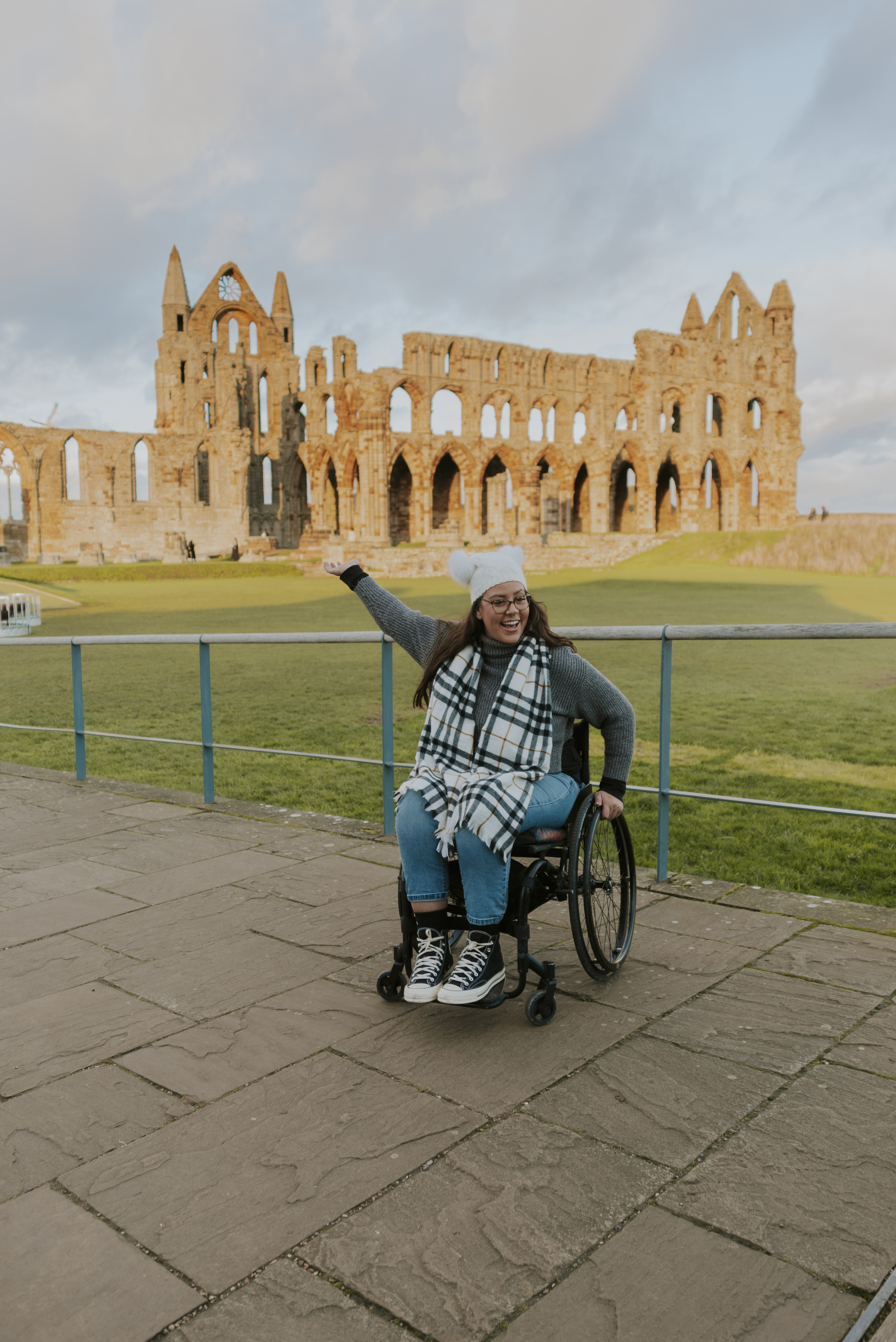 A woman in a wheelchair in front of a ruined abbey.