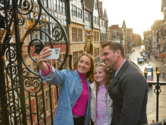 A family taking a selfie on a historic street with ornate ironwork and timber-framed buildings in the background.