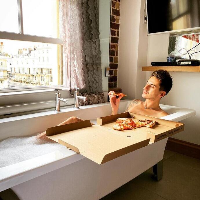 Man in bath looking out of the window eating pizza at Hotel UNA