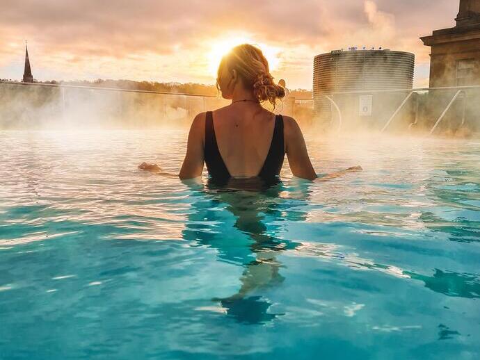 A woman stands looking out to a view in the rooftop pool at sunrise