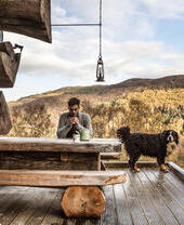 Un homme assis sur la terrasse d'un chalet en bois avec un grand chien