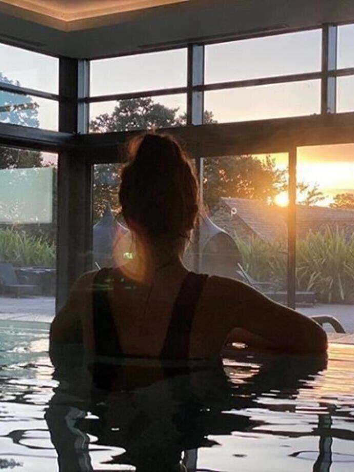 Donna nella piscina della Gaia Spa che guarda fuori dalla finestra al tramonto