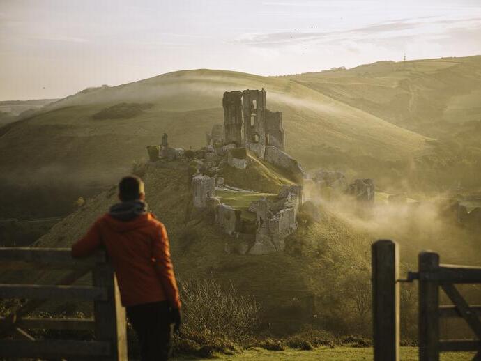 Man leaning on gatepost, looking at the ruins of a castle
