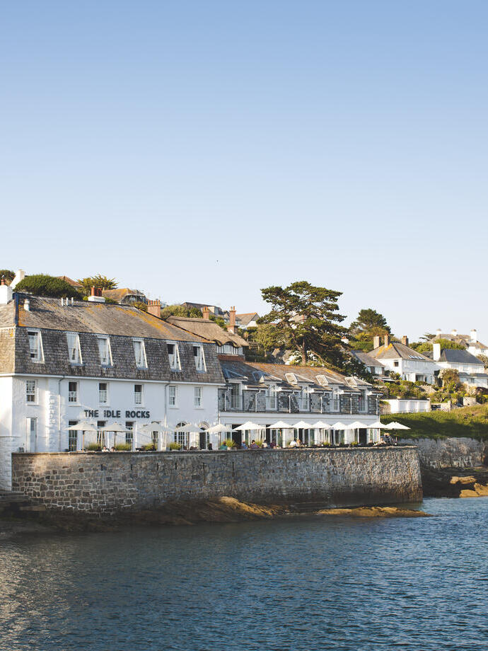 Hotel, overlooking the sea to the outside of, adjacent to a rocky cove and other white residencies along the coastline.