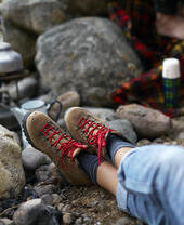 Woman sitting on a rocky ground, with legs outstretched waiting for a kettle to boil