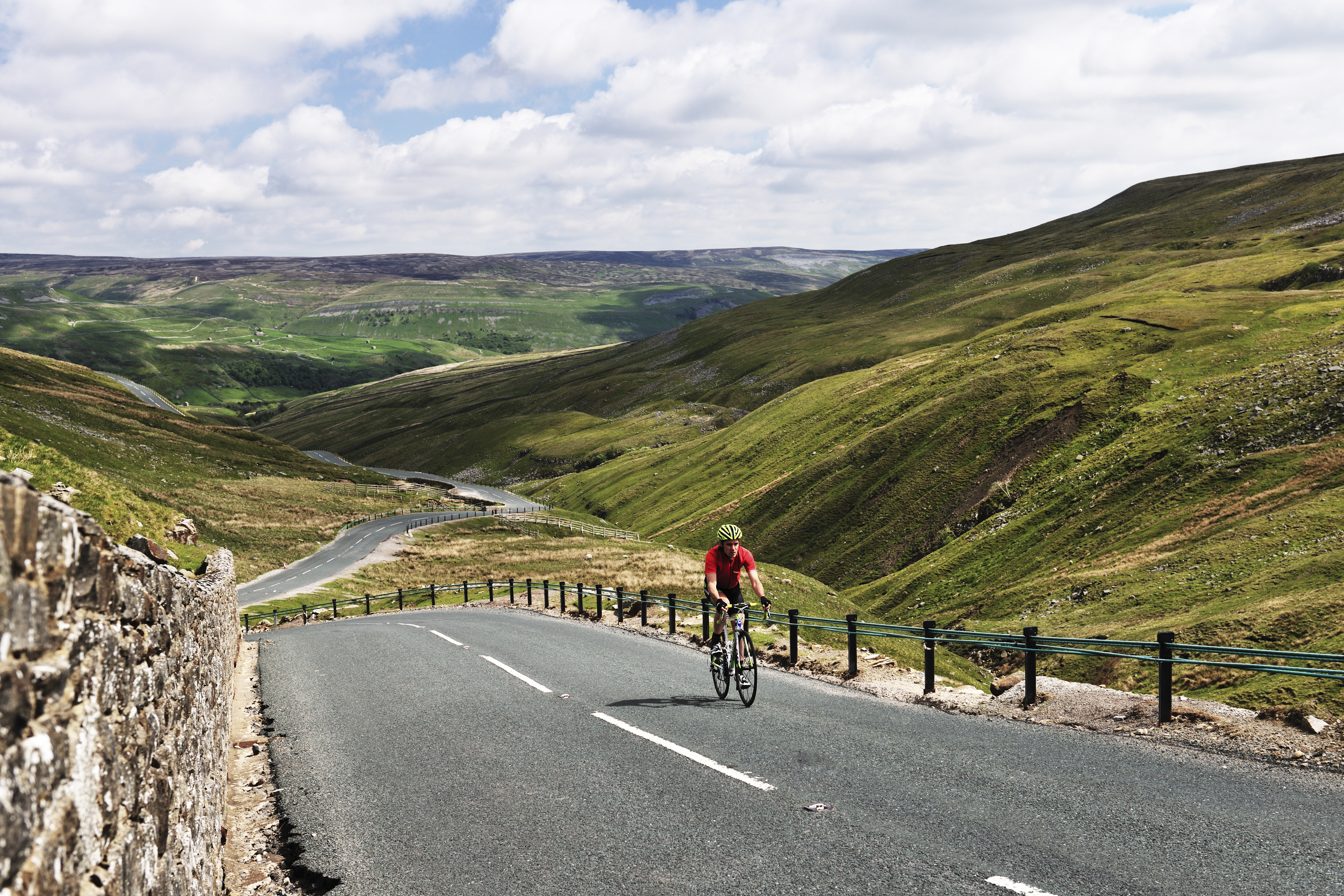 Cyclist riding on road through green dales