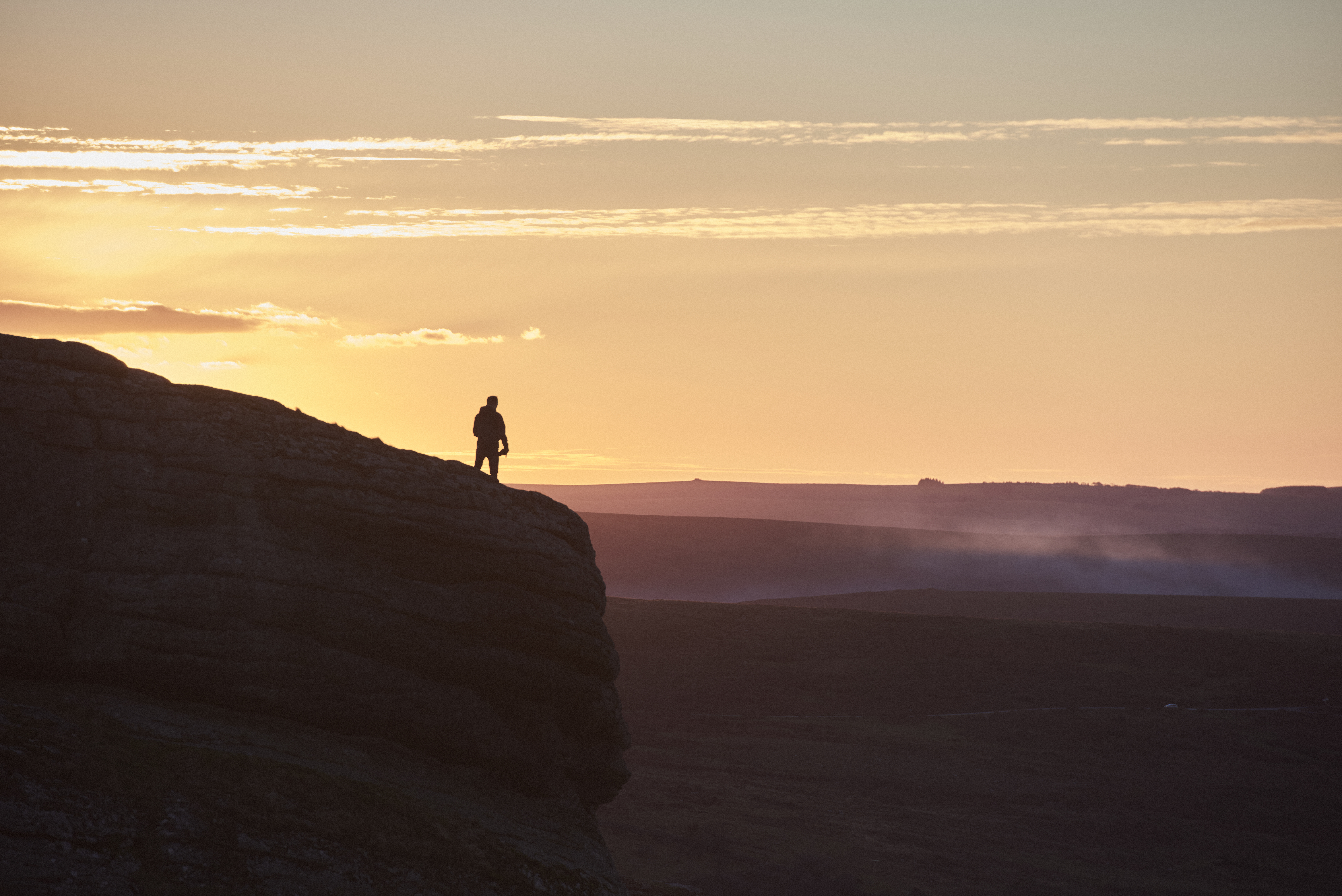 Silhouette of person hiking on large hill at sunset