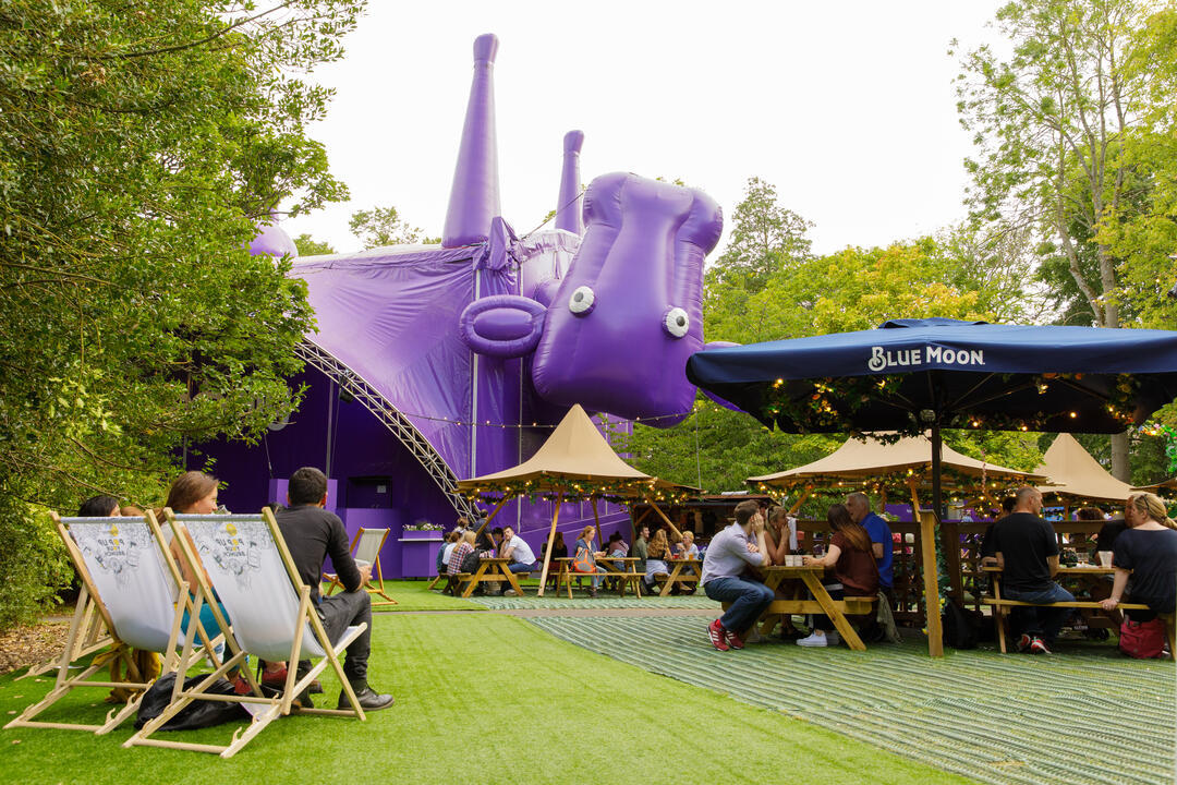 Visitors relaxing outside a tent shaped as a purple upside down cow