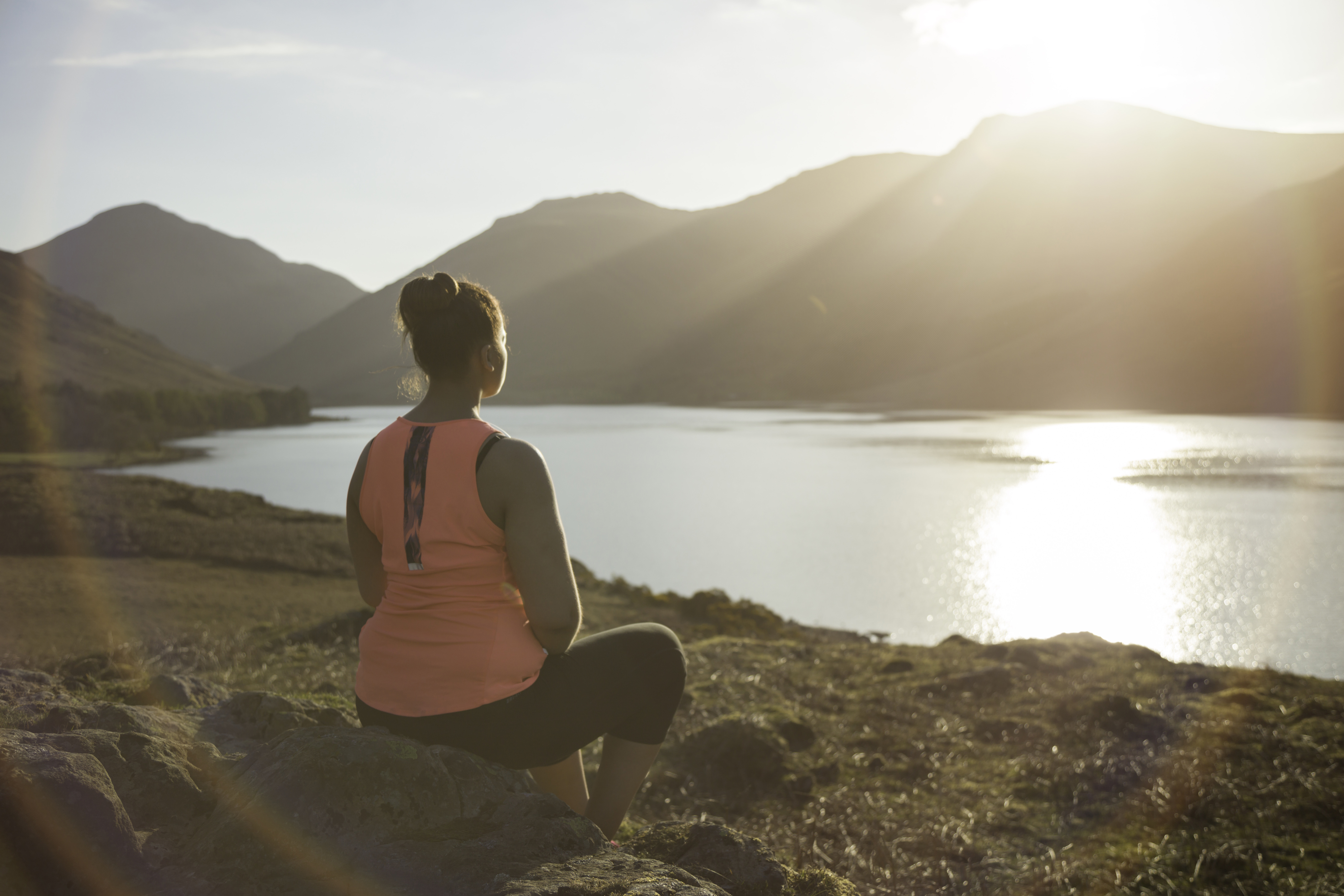 Woman, meditating in green valleys, near lake. High sun