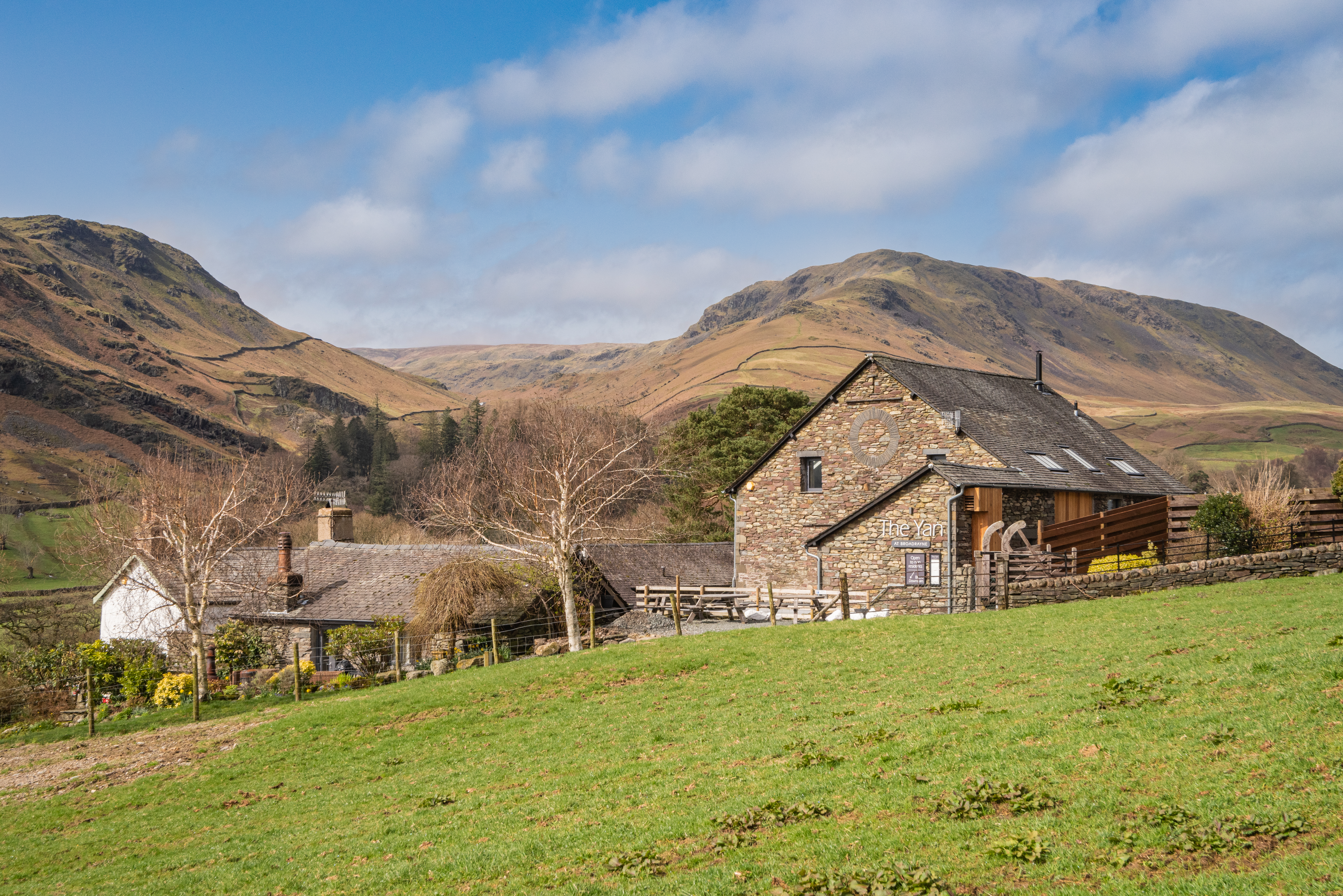 An external view across the field to some buildings, with the hills in the distance