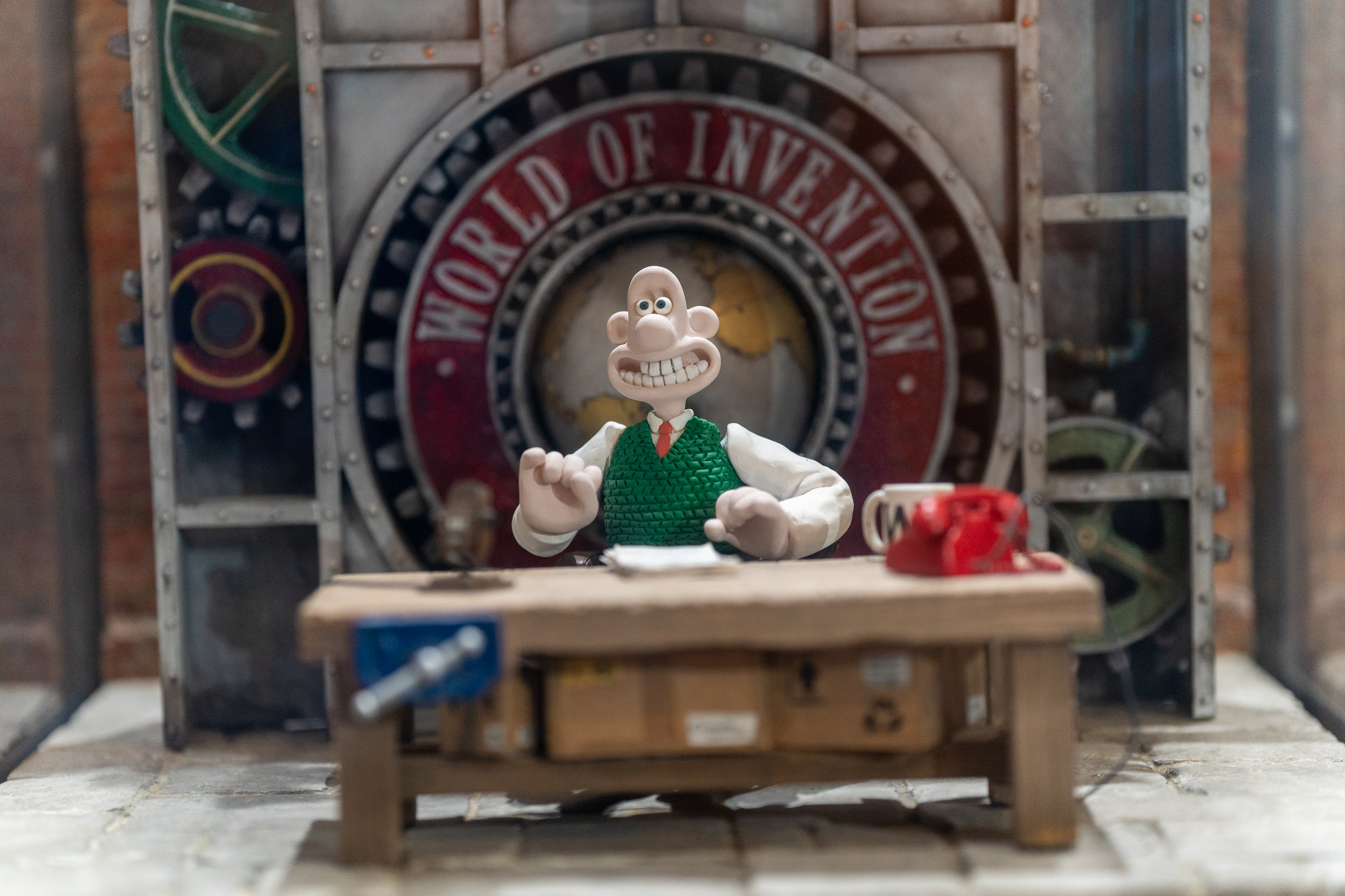 Figurine de Wallace assis à un bureau, avec une pancarte indiquant « World of Invention » (Le monde de l'invention) en arrière-plan.