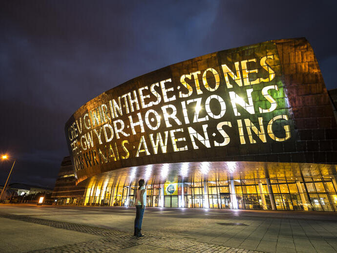 Persona mirando hacia arriba a la fachada de un edificio de bronce por la noche