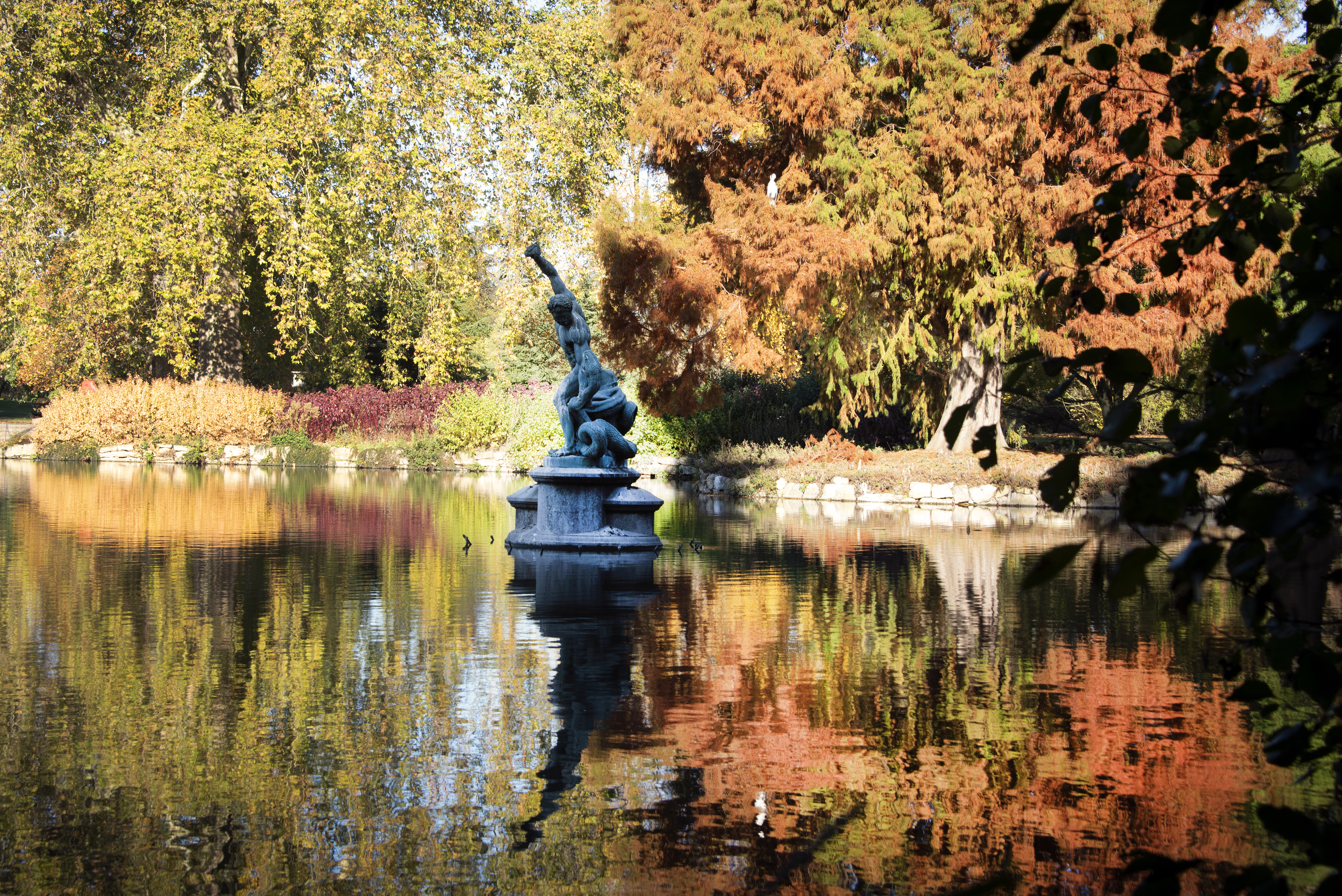 A statue in a lake surrounded by trees in autumn