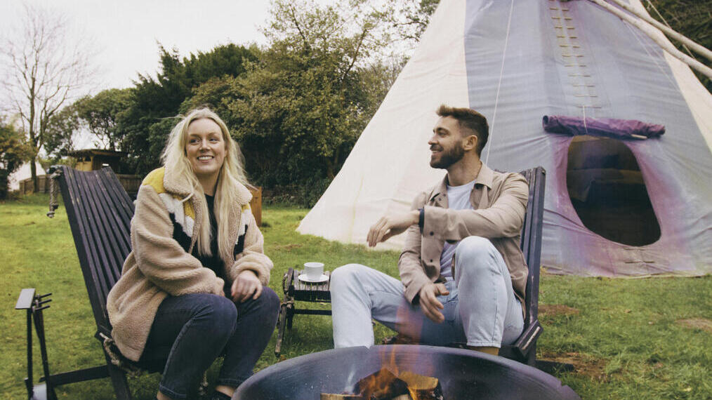 Un homme et une femme assis autour d'un feu, près d'un tipi