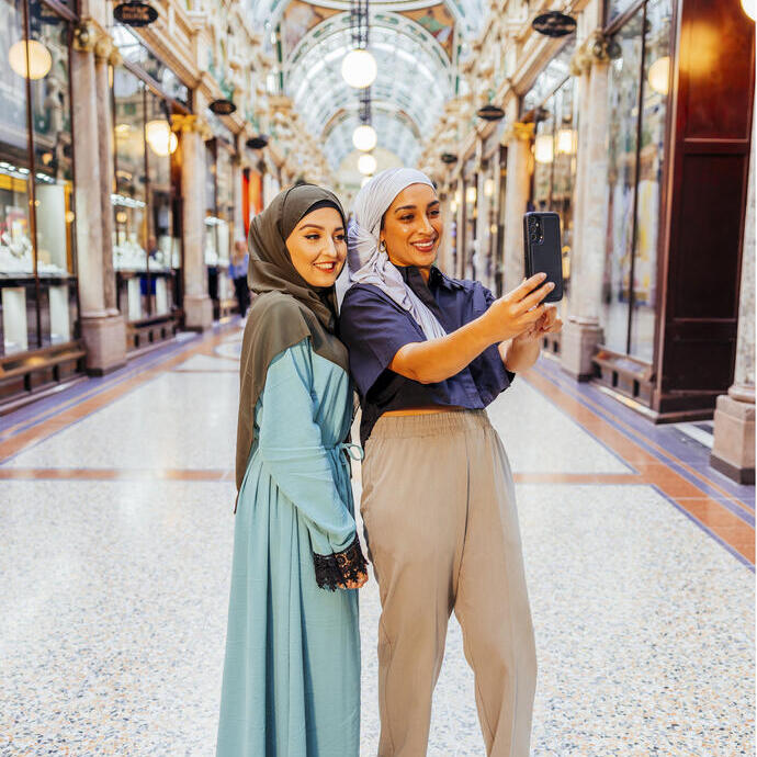 Two women take a picture together in an indoor shopping arcade