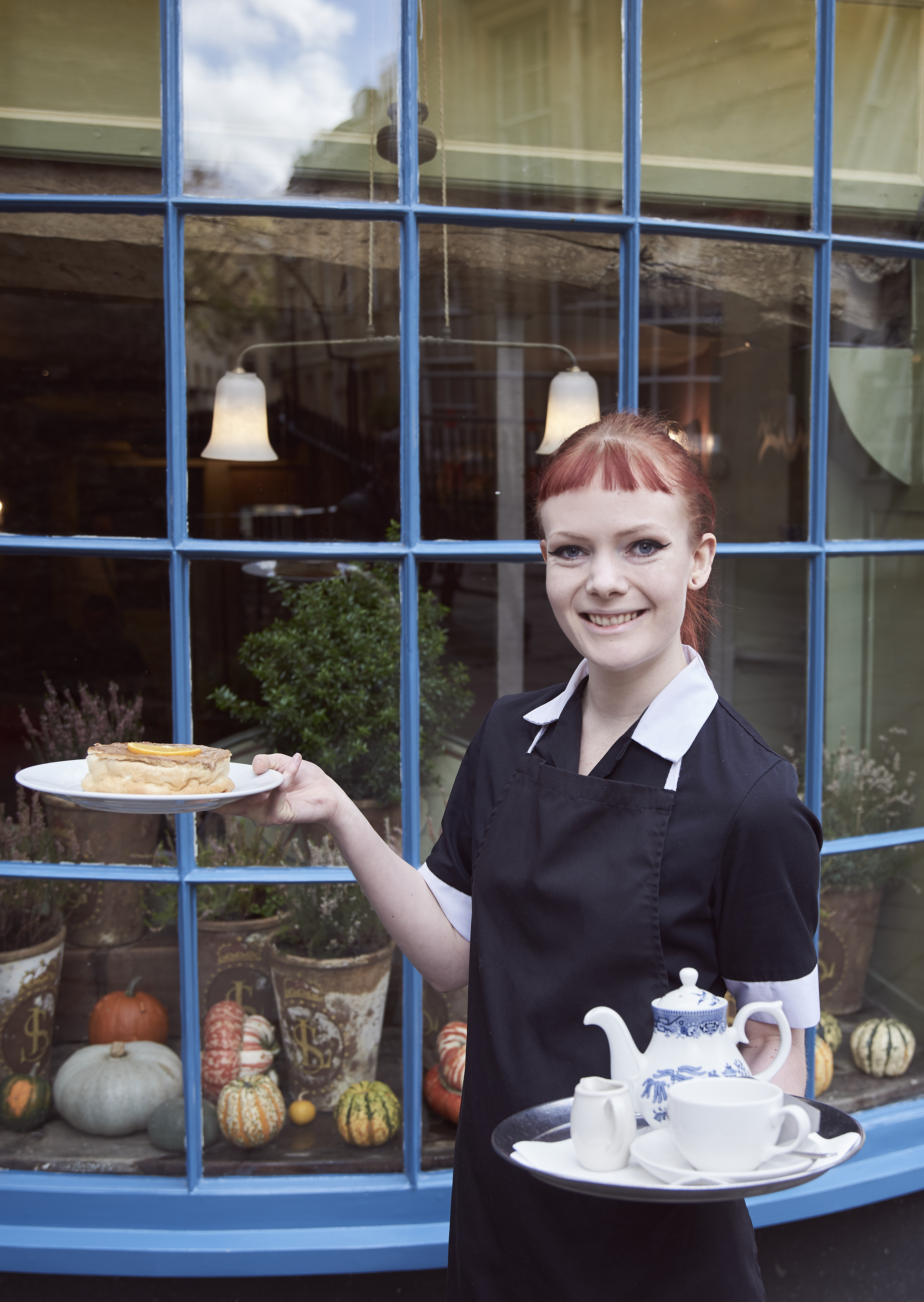 Member of restaurant staff holding a tray with tea and a cake on a plate