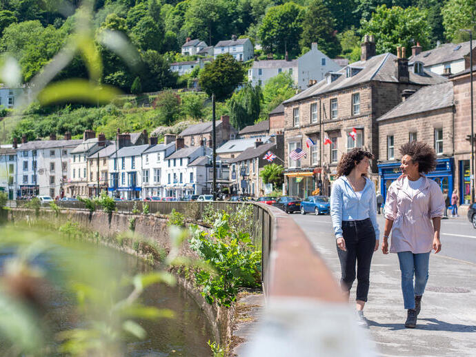 Two women walk down a main street in a hillside town