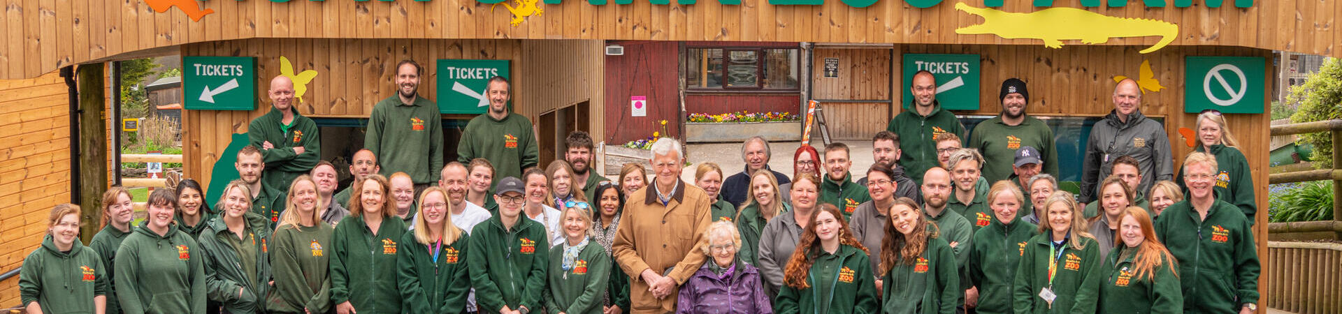 A sign which reads "Welcome to Noah's Ark Zoo Farm" with various staff members standing in front wearing matching branded tops. Noahs Ark Zoo Farm - Gold award winner for the Accessible and Inclusive Tourism Award at the VisitEngland Awards for Excellence 2023.