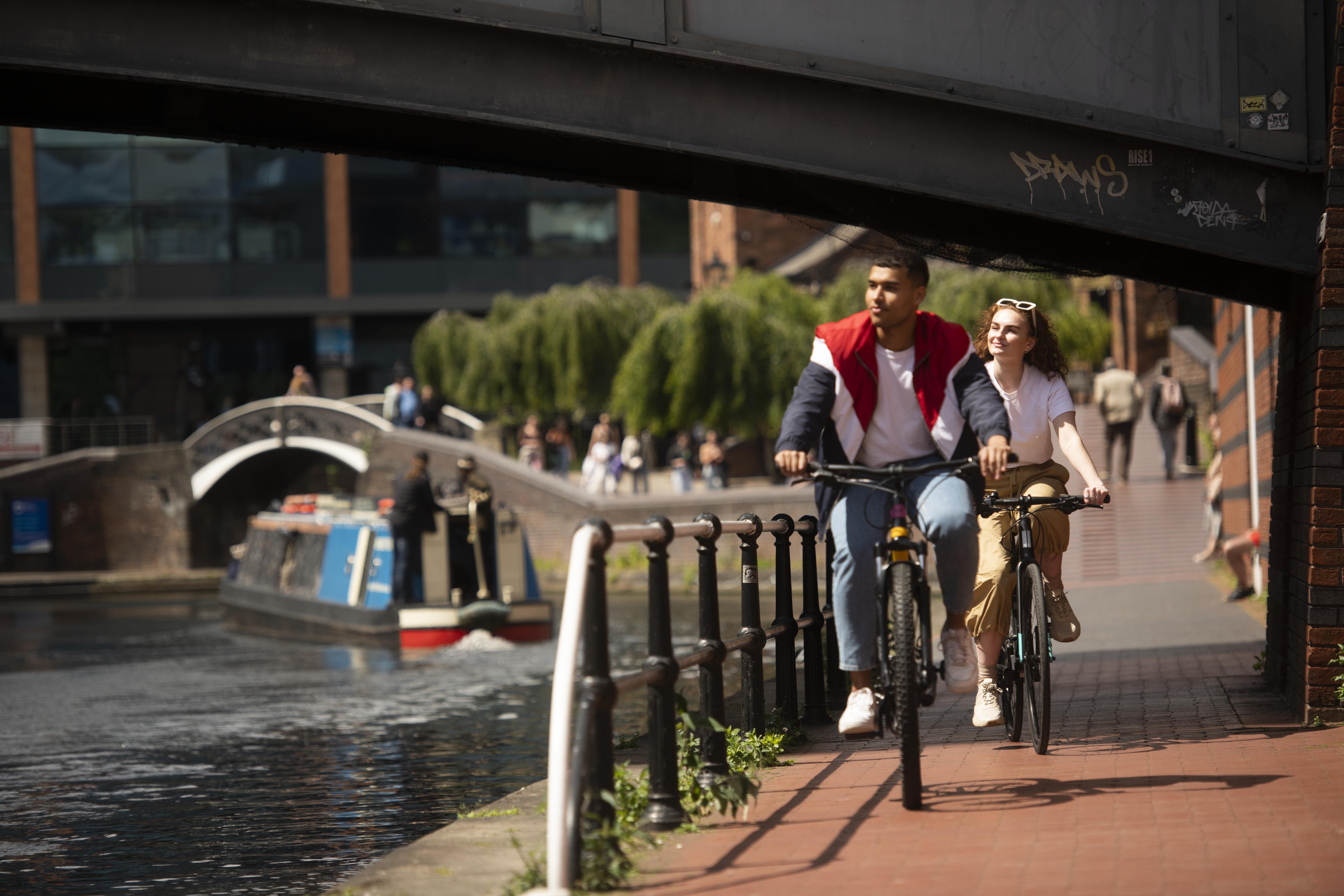 A couple cycling down a ramp parallel with a canal