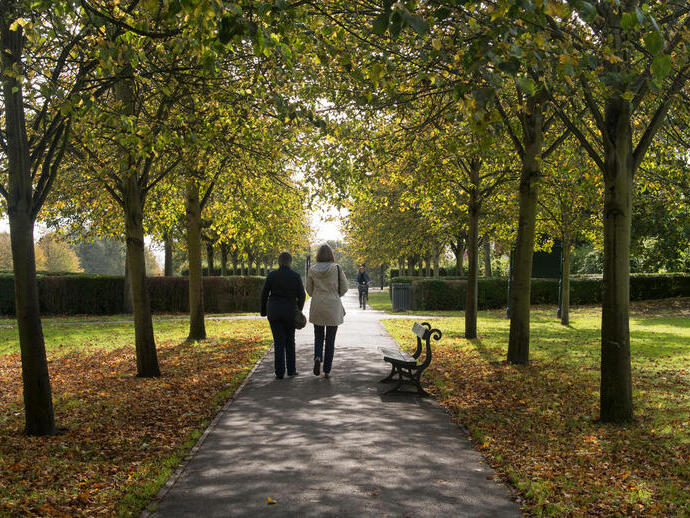 Two ladies walking through a tree lined path in Rowntree Park, York.