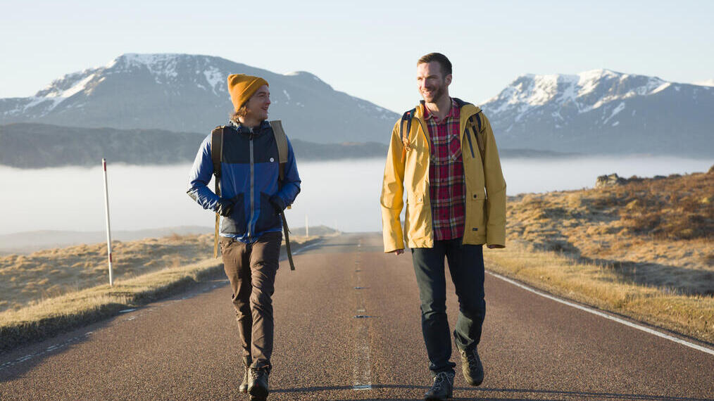 Two men hiking along a country road. Snowy mountains behind