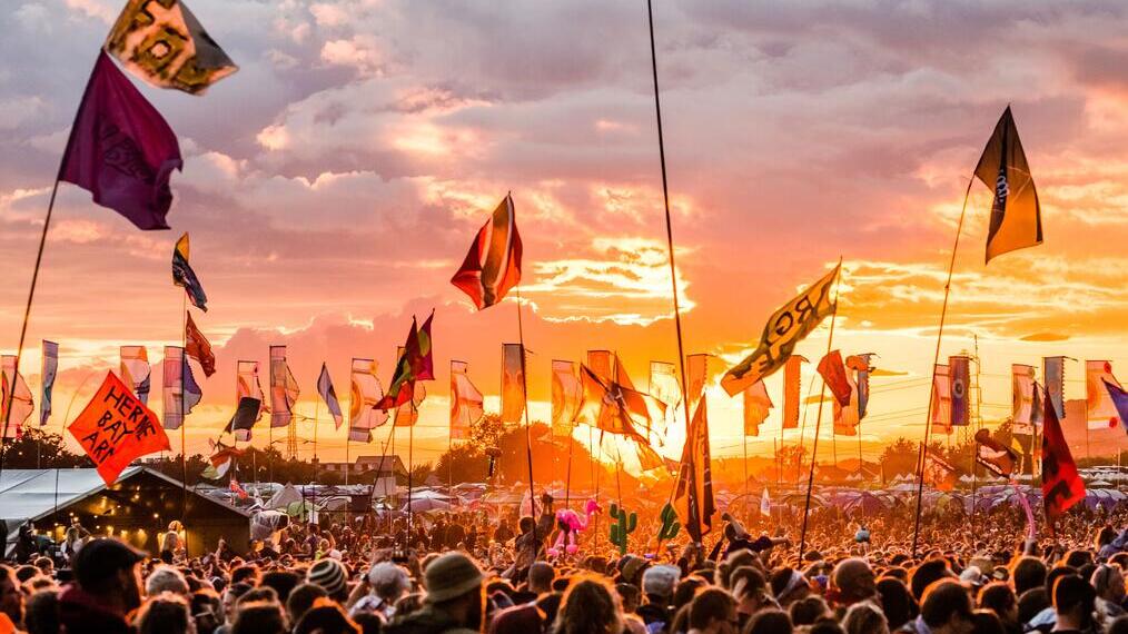 Glastonbury Festival, showing crowd of people at sunset with flags waving