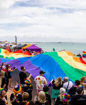 Une foule de personnes brandissant un grand drapeau arc-en-ciel sur la côte de Cornouailles