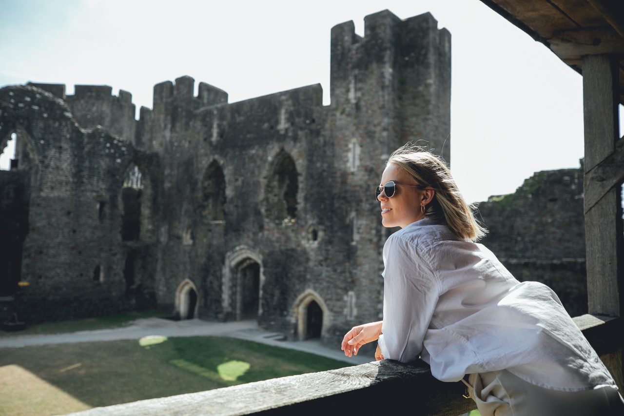 امرأة ترتدي نظارات شمسية تنظر إلى قلعة كيرفيلي، ويلز