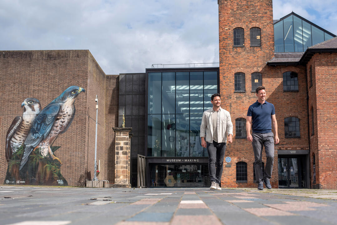 Two men walk away from a museum which has a large mural of birds of prey
