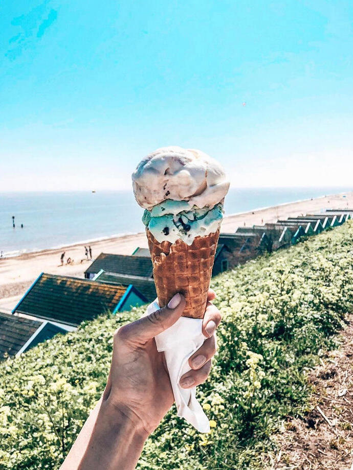 Person holding ice cream cone with view of row of beach huts
