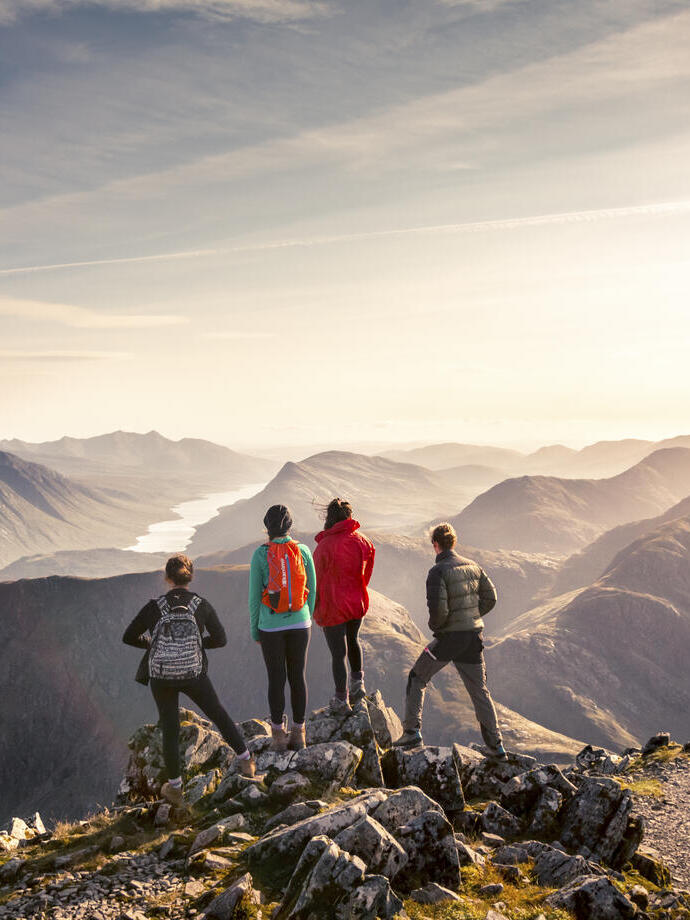 A group of people standing on high point looking at the mountain view below