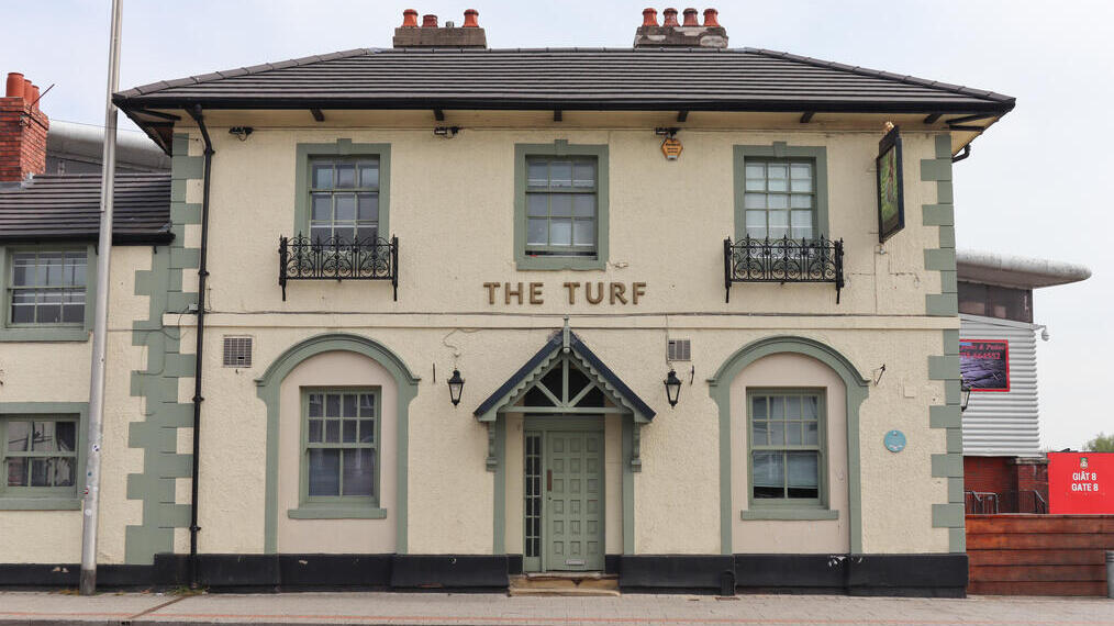 Entrada a un pub británico con un cartel que dice «The Turf».