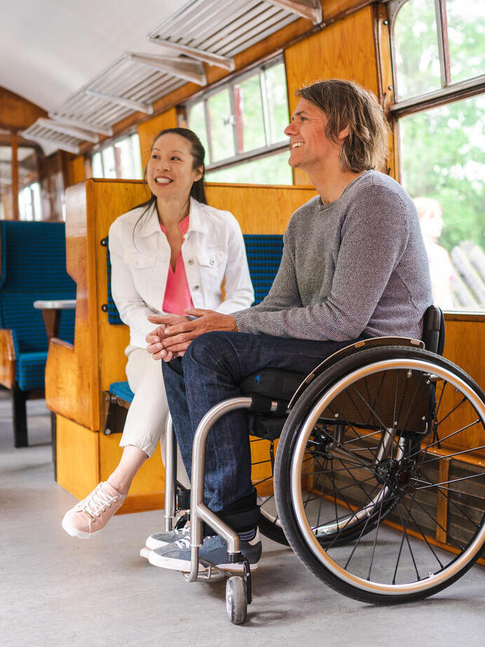 Man sitting in a wheelchair next to woman sitting on seat in accessible carriage on heritage train