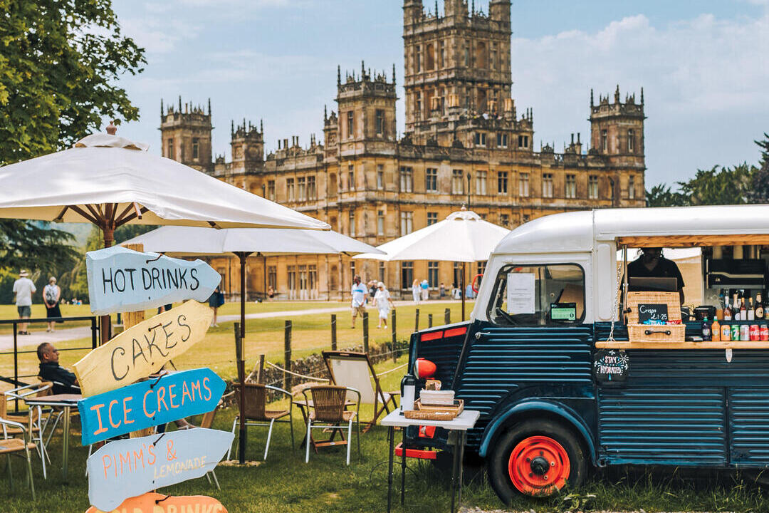 Ein Imbisswagen, Sonnenschirme und Wegweiser auf dem Gelände einer Burg