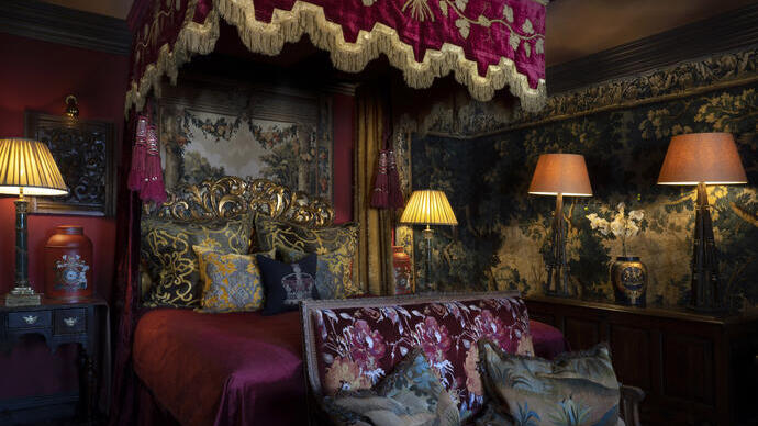 Ornate vintage bedroom with rich fabrics, a canopy bed, brocade cushions, floral wallpaper, and warm ambient lighting.