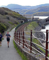 Two people running along a coastal path in Wales